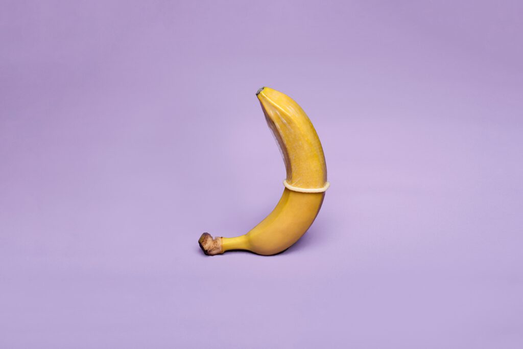 pexels-photo-5915349-5915349 A banana wearing a condom symbolizes safe sex education against a pastel purple background.
