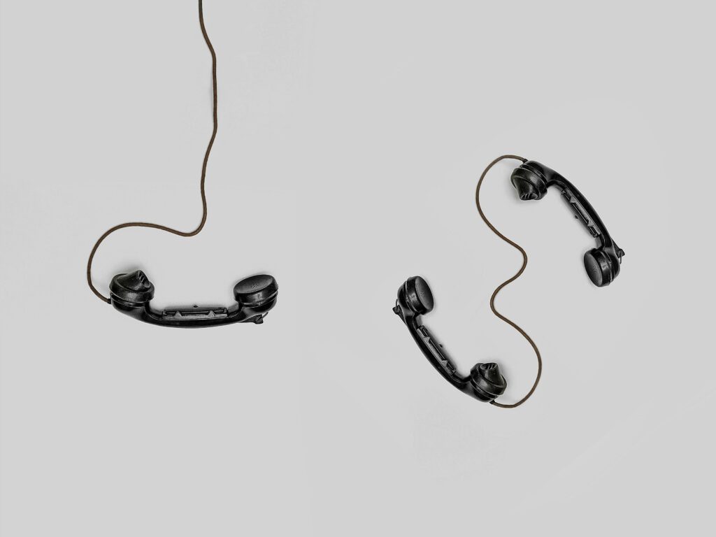 pexels-photo-821754-821754 Two vintage black telephone handsets connected by cords on gray background.